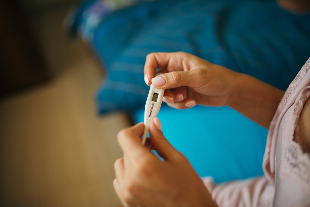 Ein digitales Fieberthermometer liegt neben einer Tasse auf einem hellen Tisch