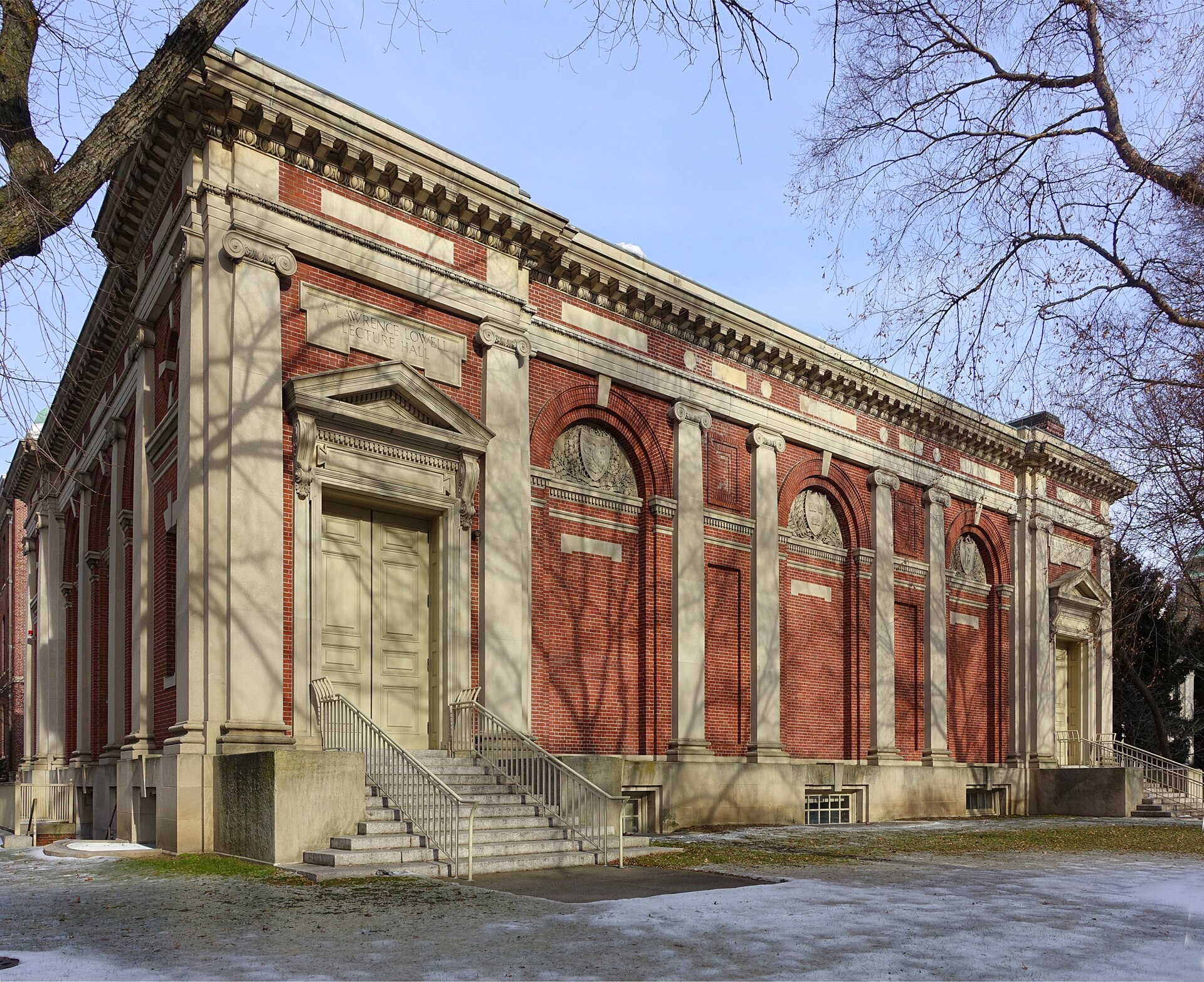 Leerer Hörsaal mit ansteigenden Sitzreihen, hölzernen Klapptischen und einer Tafel an der Stirnwand