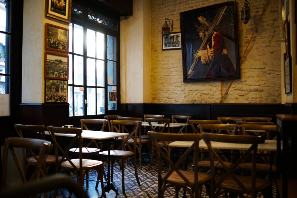 Innenraum eines Cafés mit langen Holztischen, Bänken und Hängelampen über der Sitzgruppe