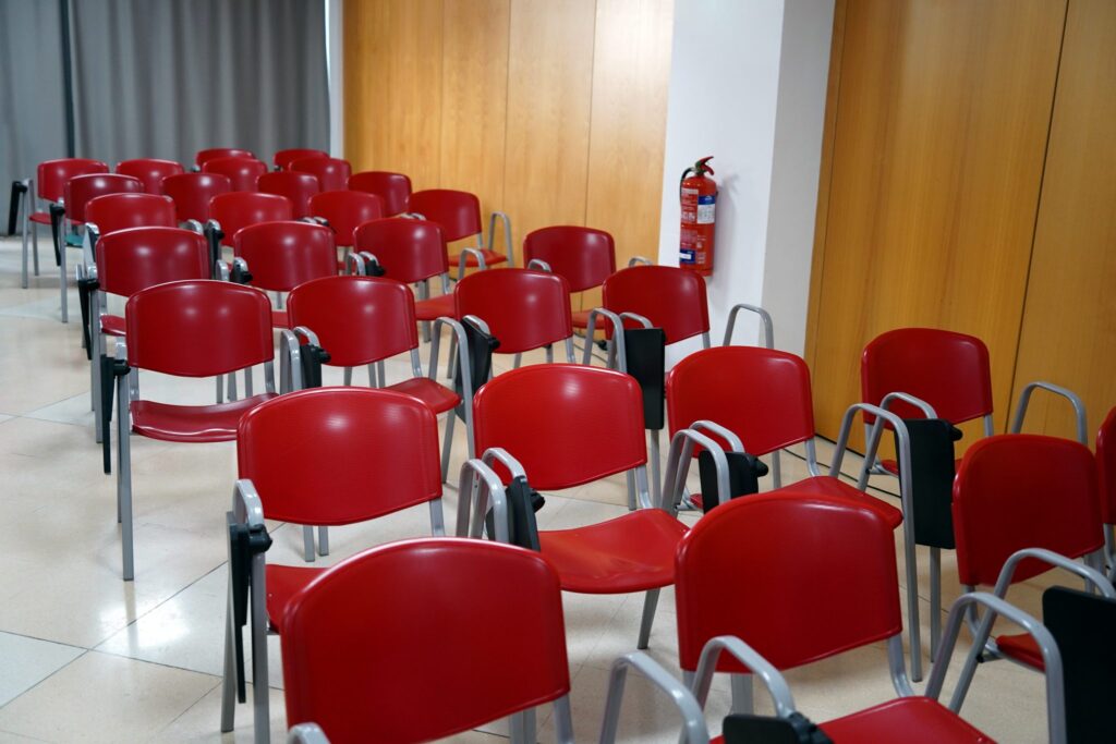 Reihen leerer Stühle in einem Seminarraum, vorne ein Projektor und eine helle Leinwand
