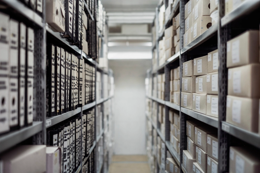 Lange Regalreihen mit beschrifteten Archivkartons in einem gleichmäßig ausgeleuchteten Kellerarchiv