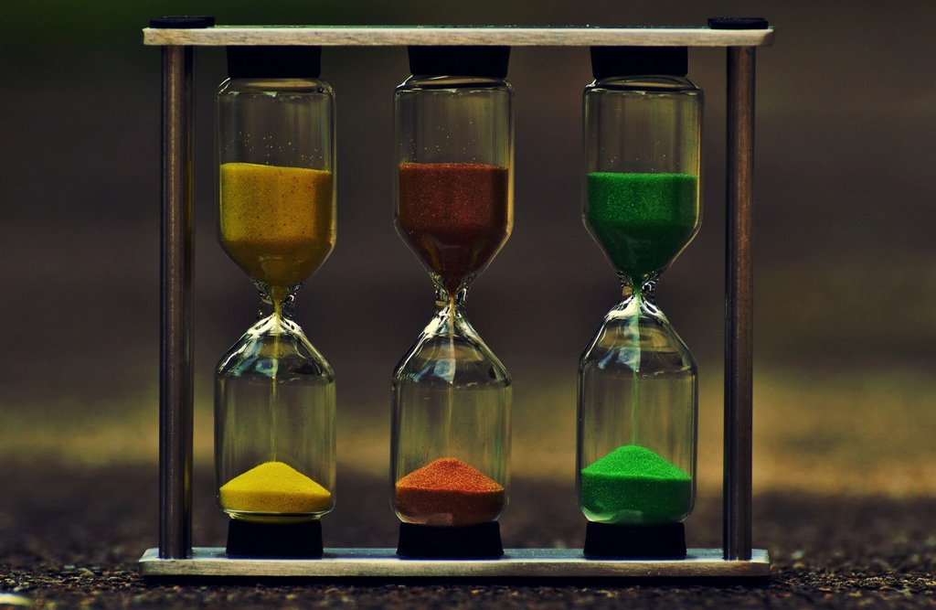Sanduhr aus Glas mit rieselndem Sand auf einer hellen Tischplatte vor neutralem Hintergrund