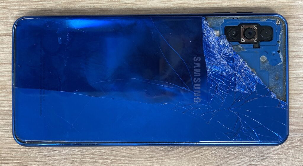Ein Mobiltelefon mit gesprungenem Bildschirm liegt auf einer dunklen Tischplatte