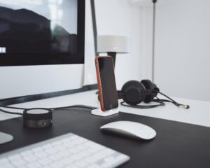Ein Headset liegt neben einer Tastatur und einem Notizblock auf einem hellen Schreibtisch