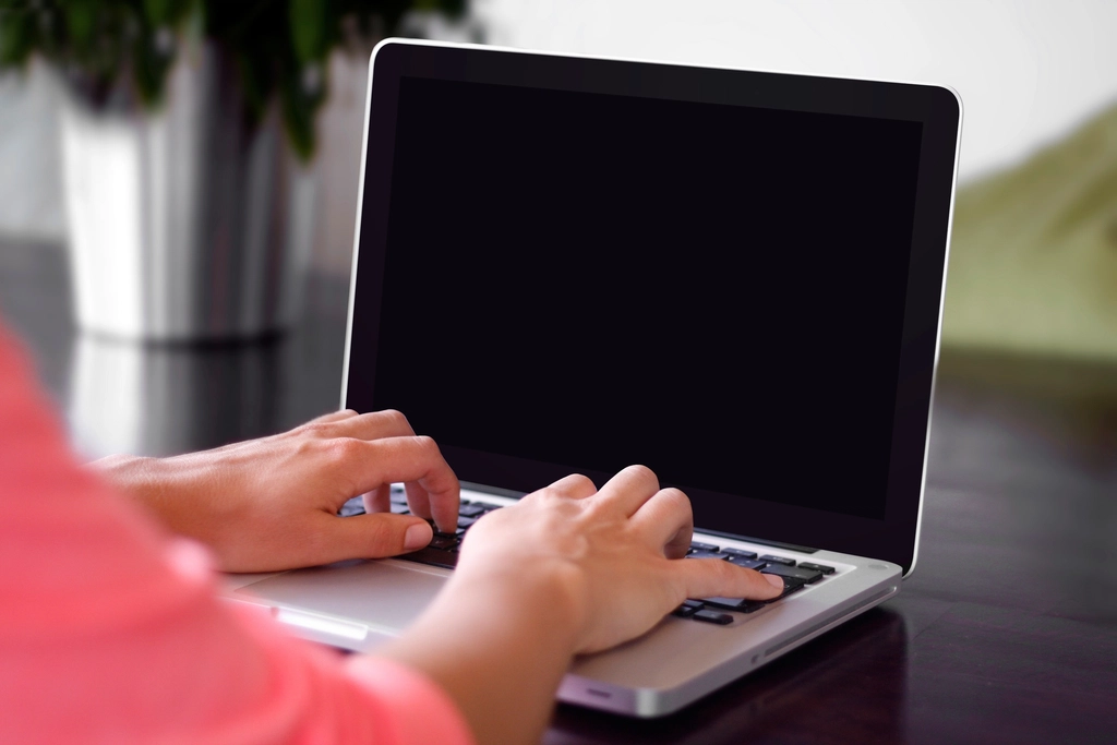 Zwei H&auml;nde tippen auf der Tastatur eines aufgeklappten Laptops
